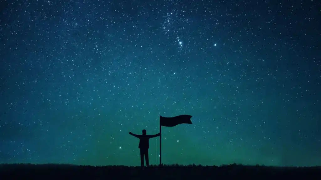 Silhouette with a flag under a starry sky – representing overcoming inner obstacles and personal growth in The Last Hour Experience.